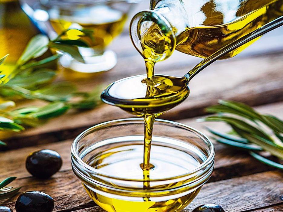 Huile d'olive versée sur une cuillère, olives et rameaux autour