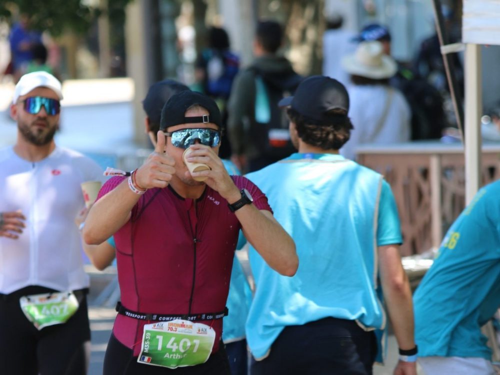 Coureur sur le parcours à pied d'un triathlon, pouce levé, et en train de boire
