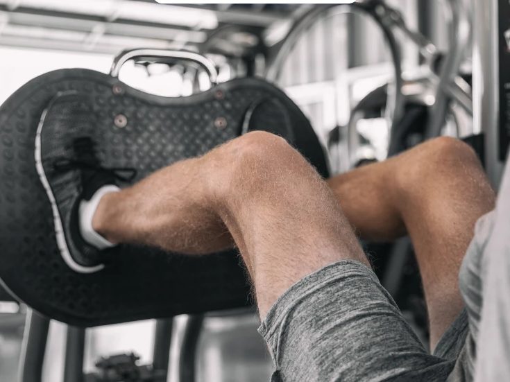 Athlète poussant la plaque d'une presse à cuisses en salle de musculation